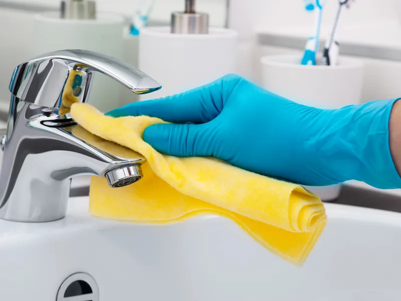 Wiping down a bathroom tap during a regular home clean in Perth